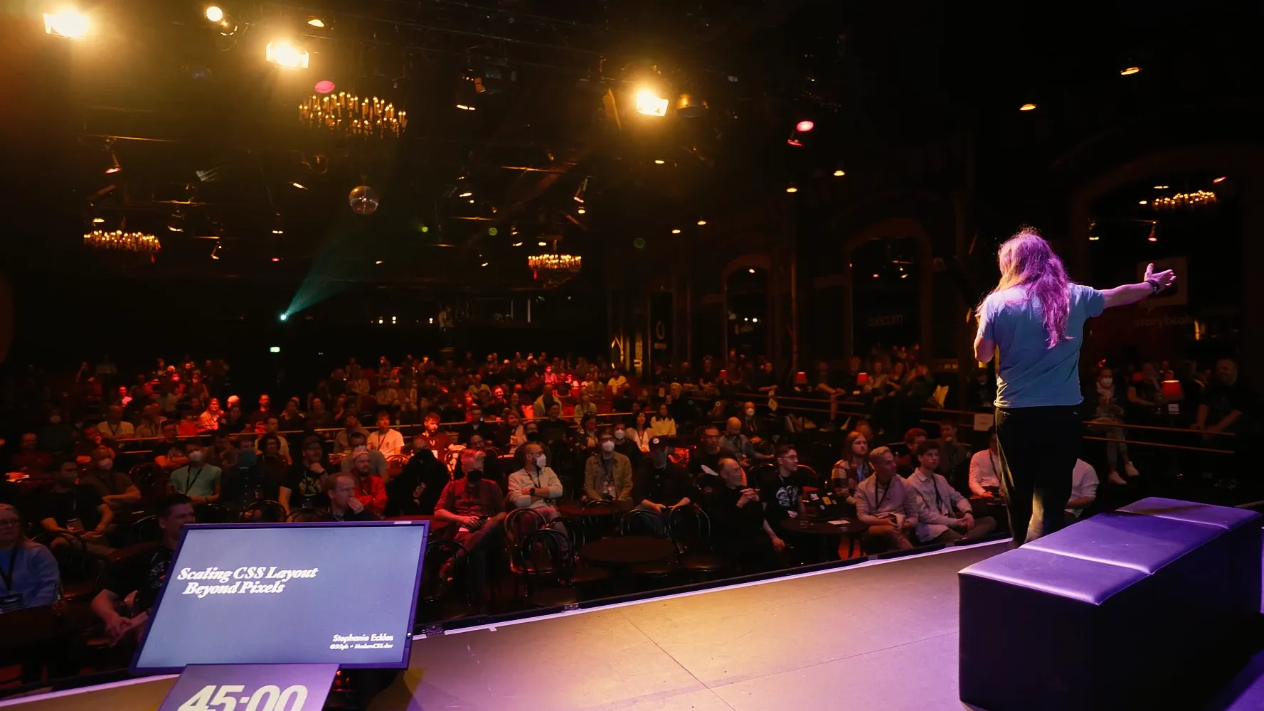 Marc Thiele on stage seen from behind, arms open to a packed, warmly lit hall