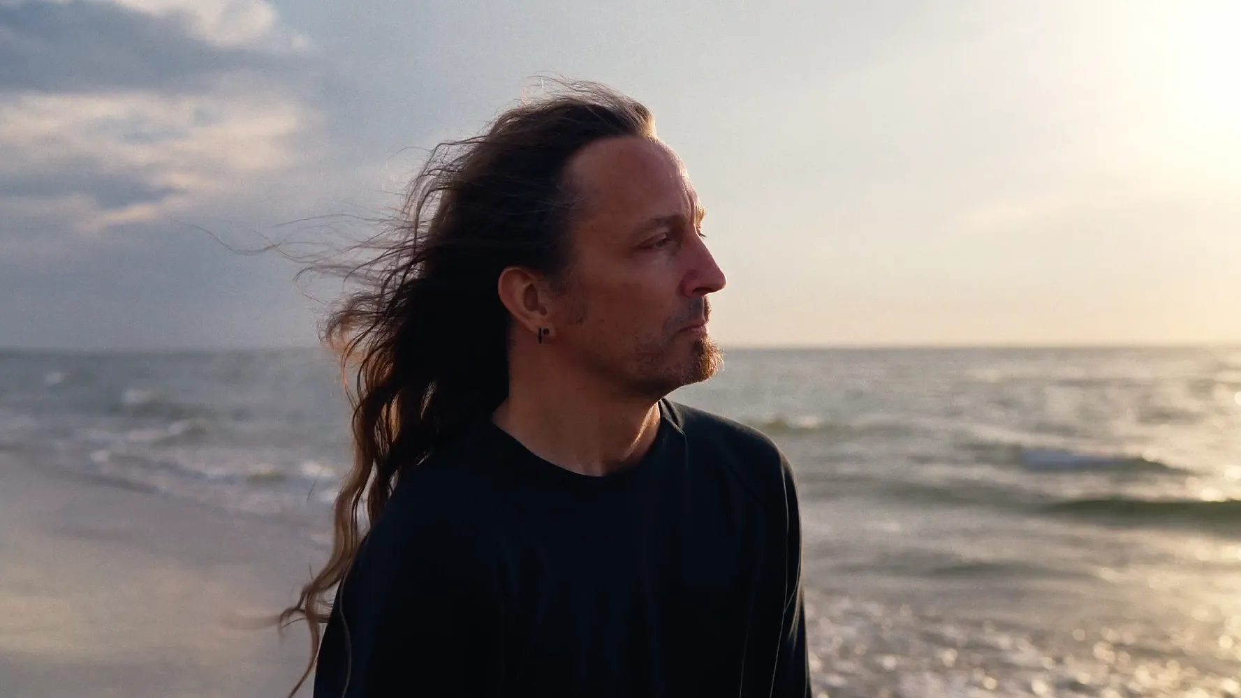 Marc Thiele alone at the shore, wind in his long hair, looking out over the water