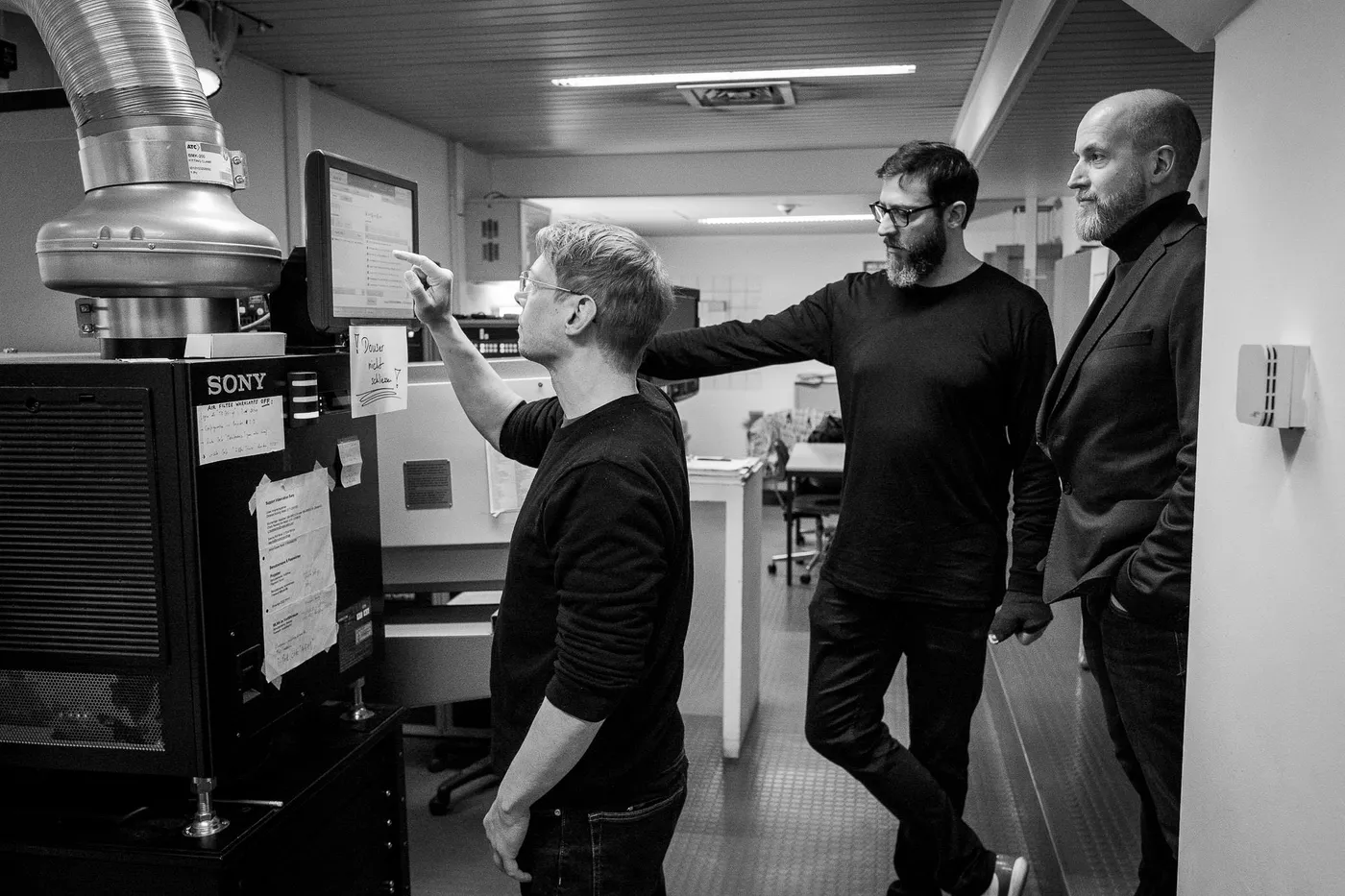 Three people in the projection booth, one pointing at a screen