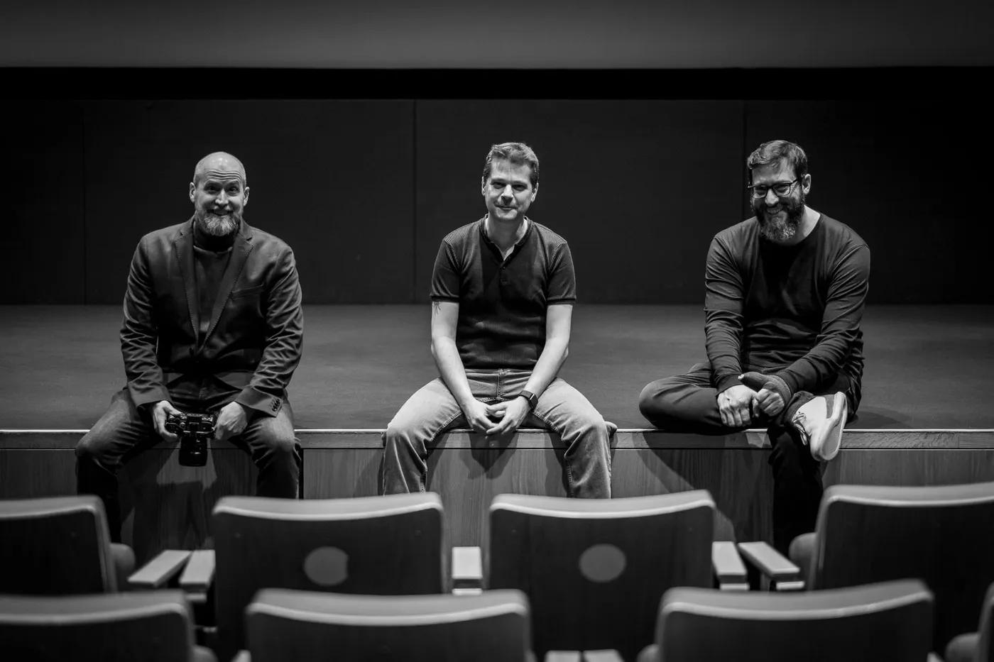 Three members of the team sitting on the edge of the stage in the empty auditorium