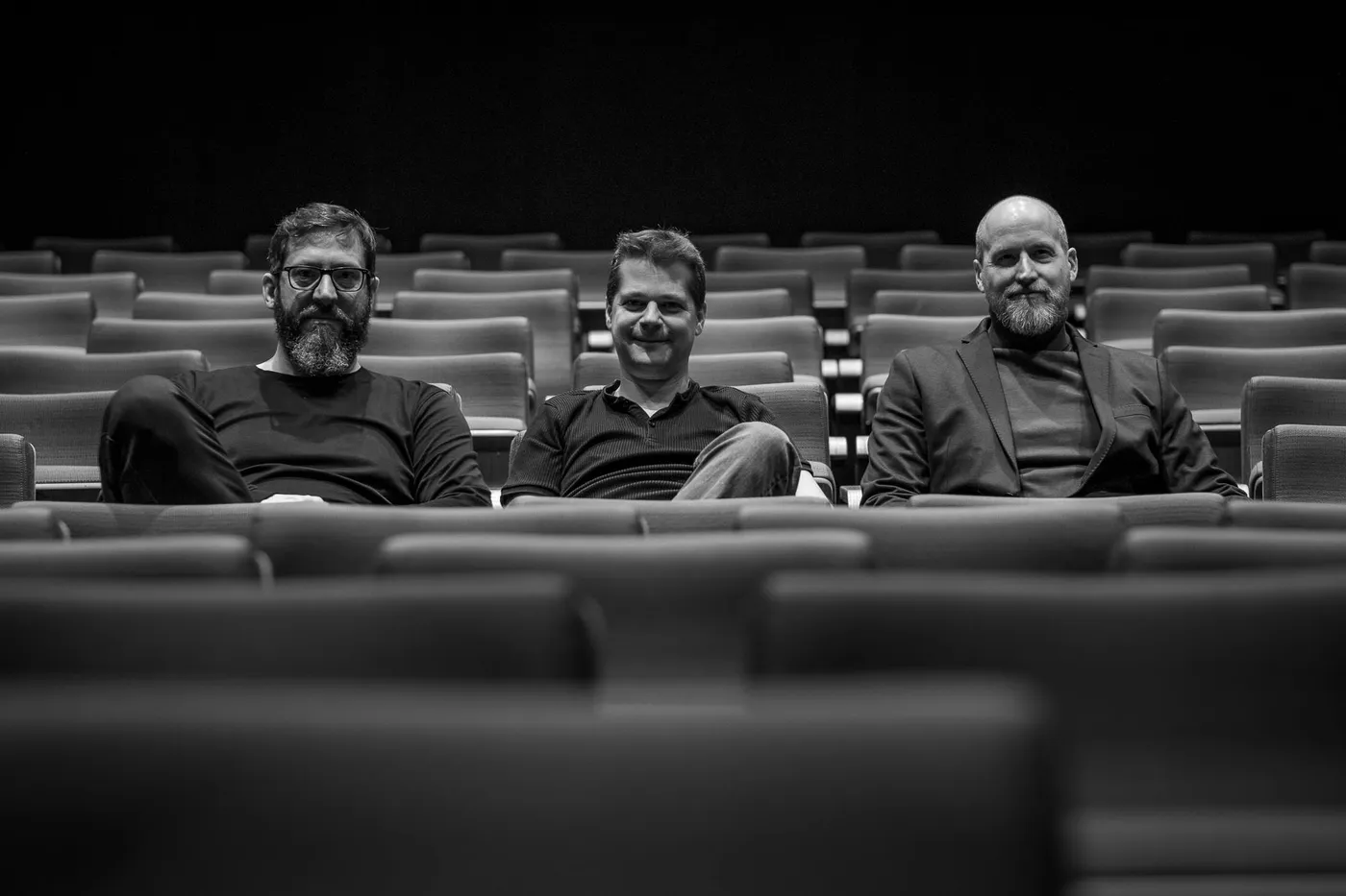 Three members of the team waiting in the empty auditorium, seen over the seat backs