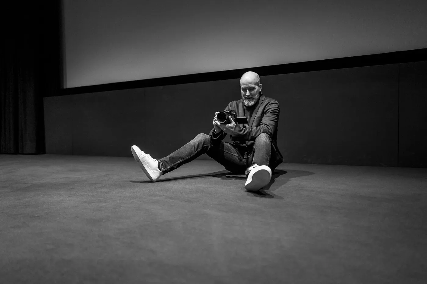 A photographer sitting on the auditorium floor with a camera, the screen behind