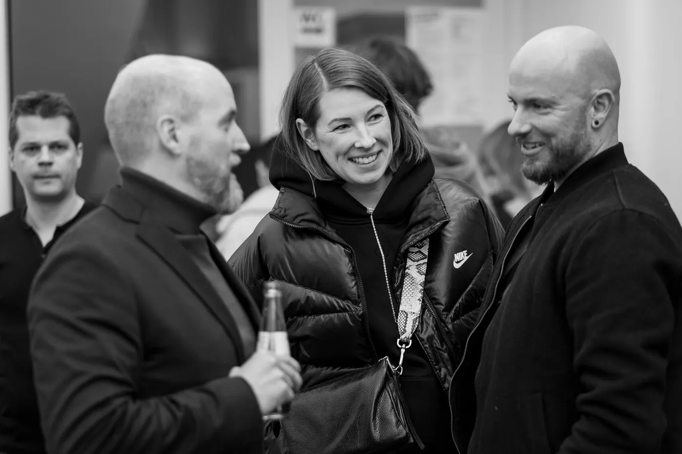 A team member and two guests greeting each other, one holding a bottle
