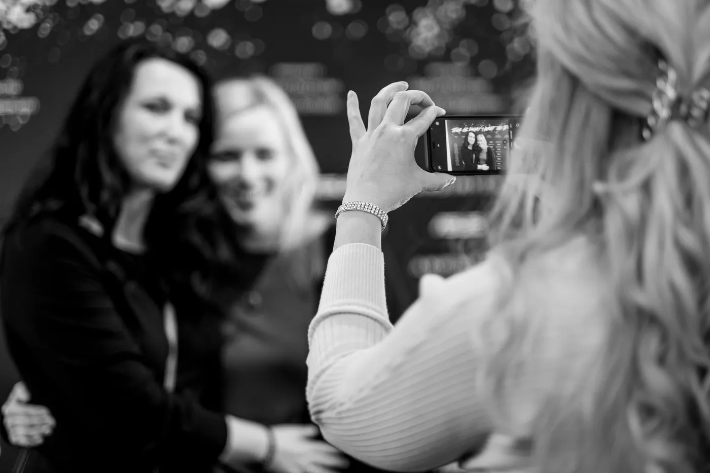 A guest taking a phone photo of two women in front of the credits wall