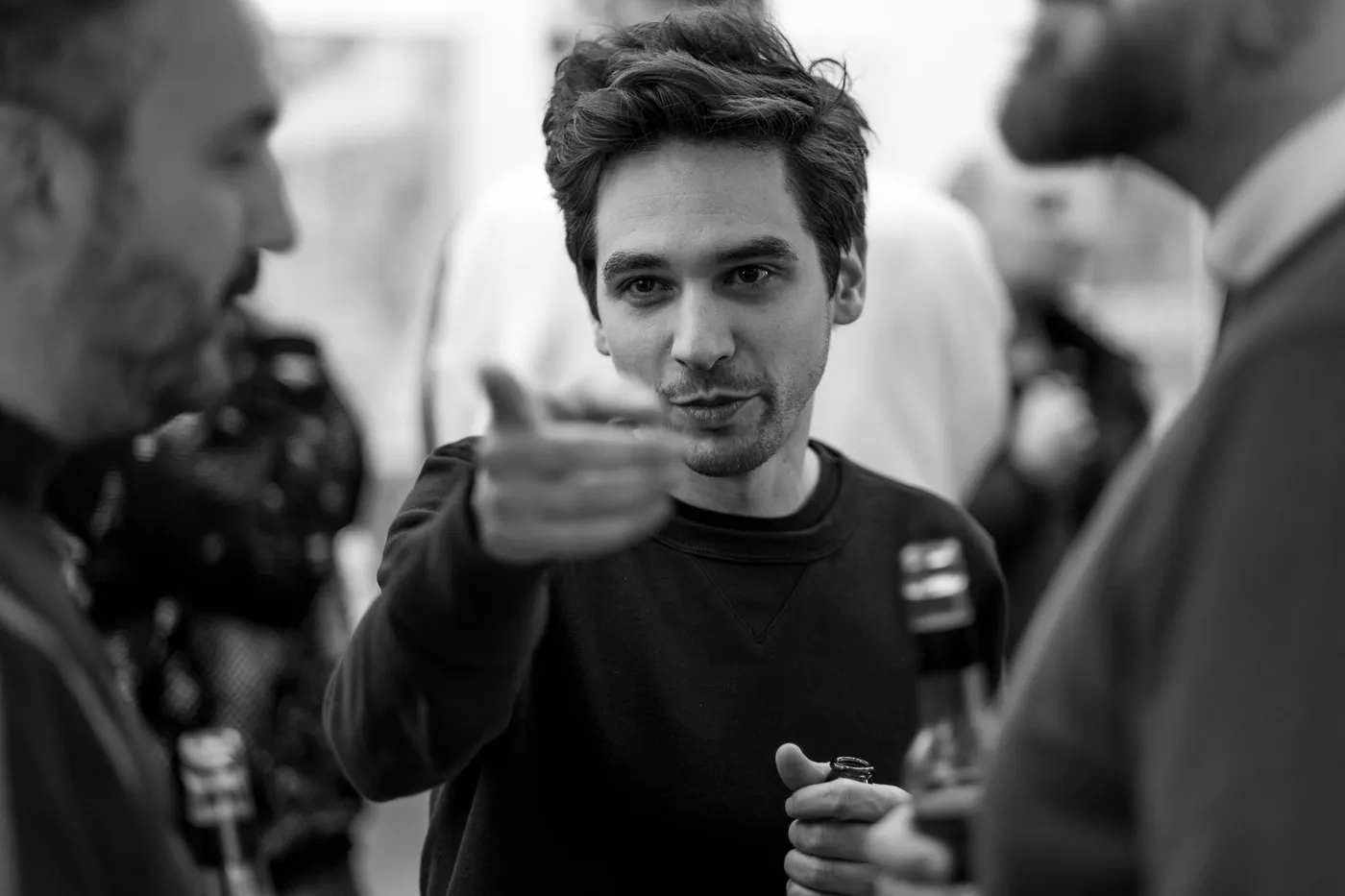 A guest gesturing mid-sentence in the foyer, a bottle in hand