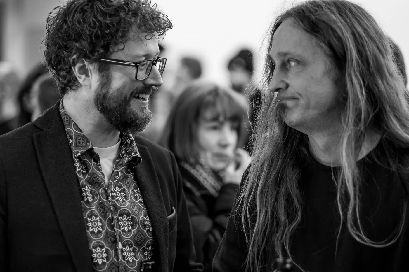 Two guests smiling in conversation, one with curly hair and glasses