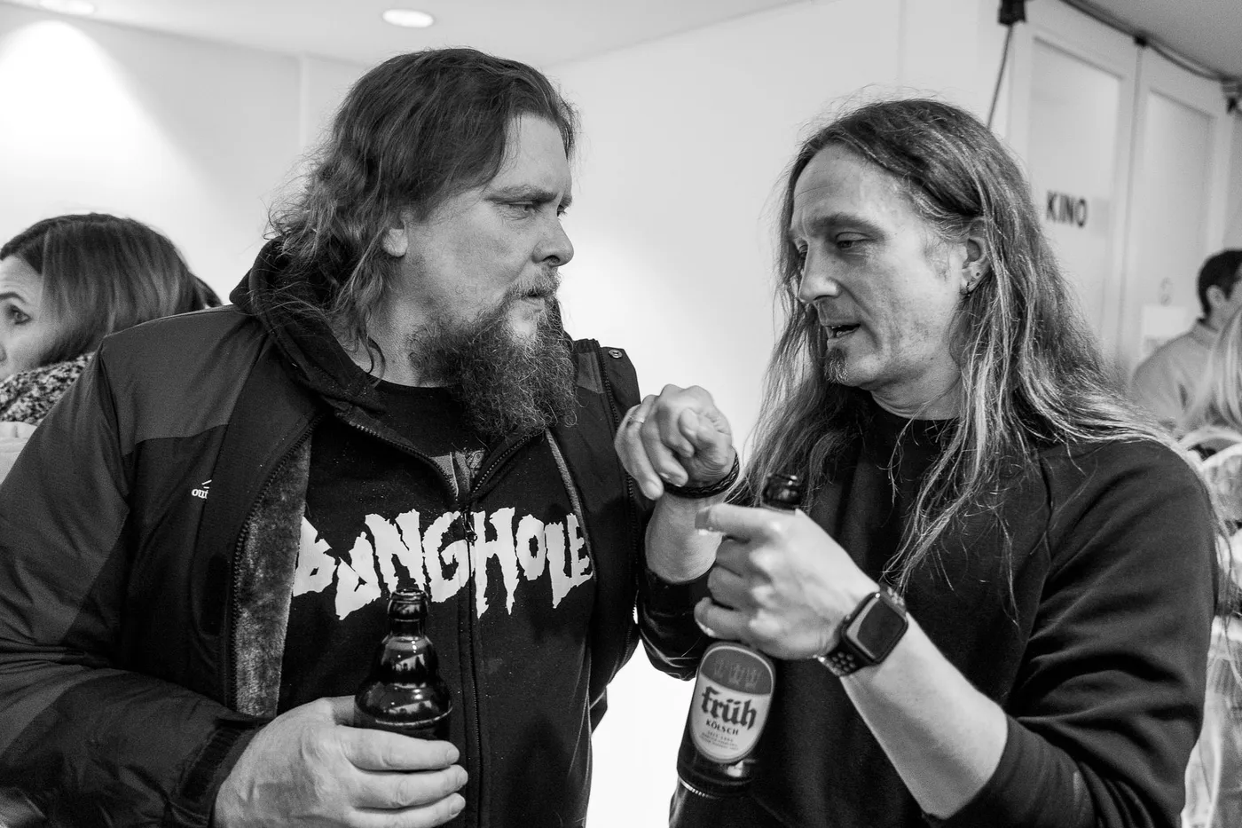Two long-haired guests toasting with bottles in the foyer
