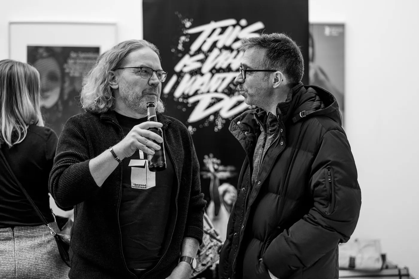 Two guests talking with bottles in front of the film’s roll-up banner