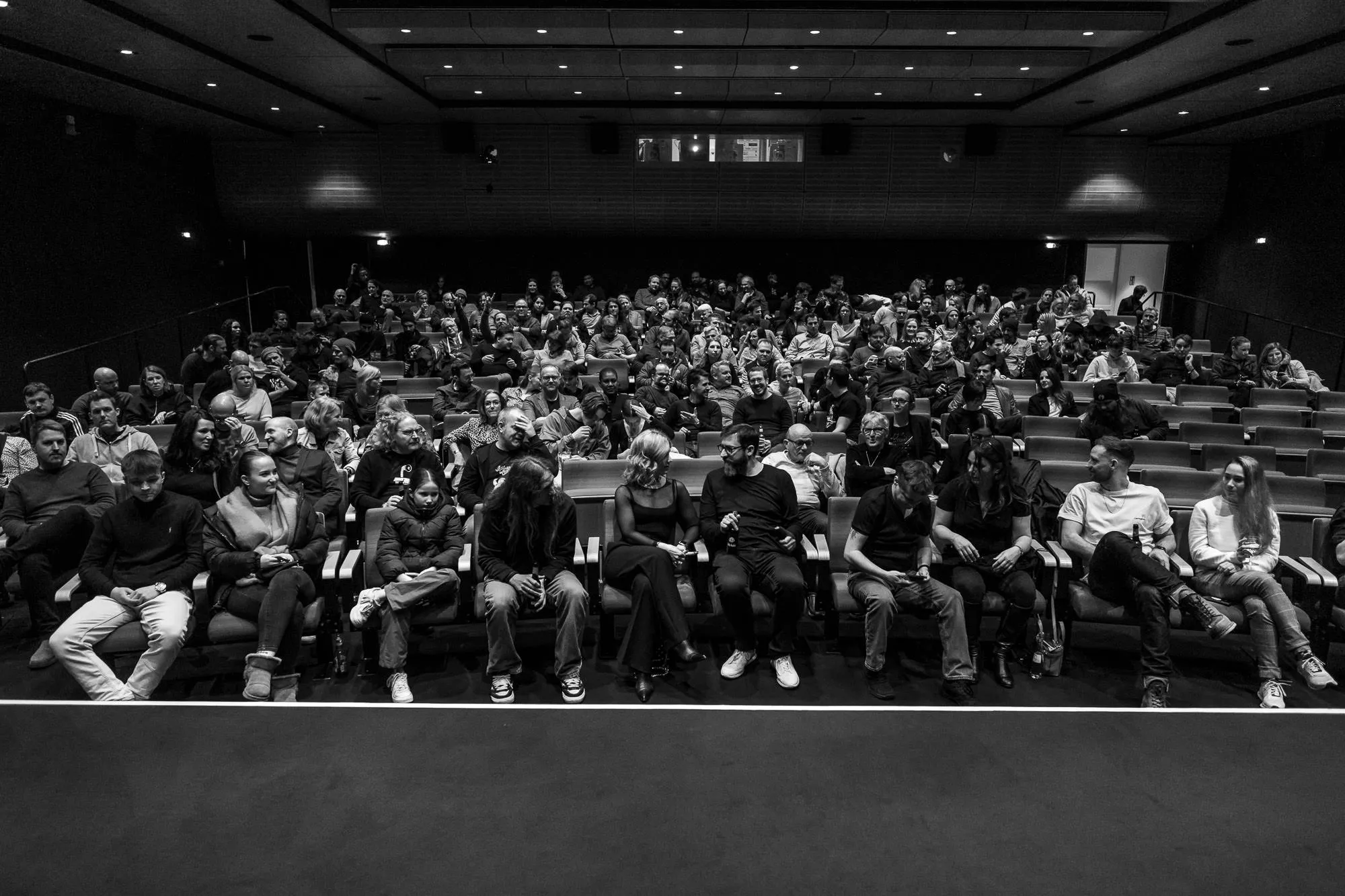 The whole hall in one wide frame from the stage, the rows rising into the dark