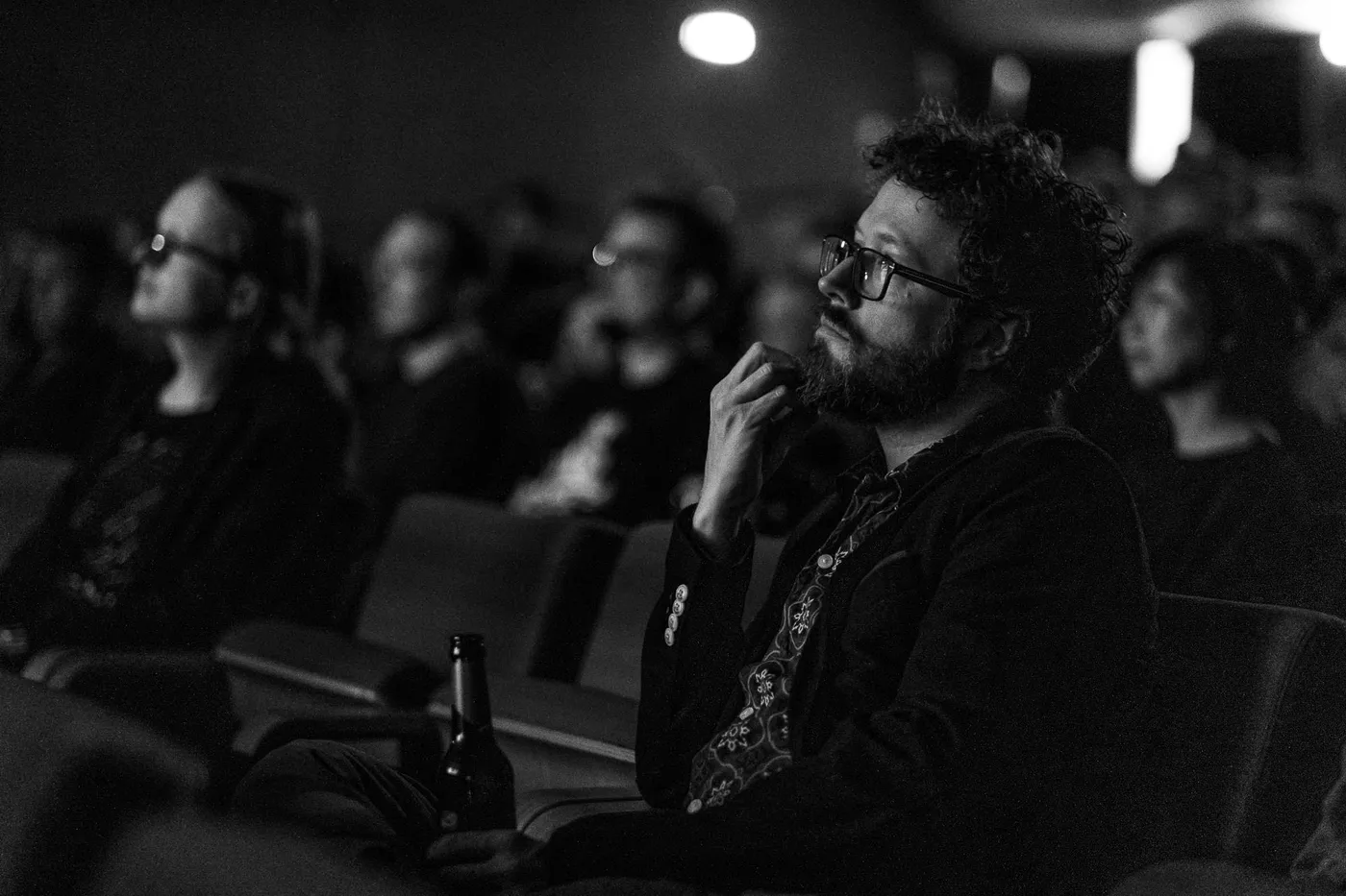 The host watching the film from the audience in the dark, his chin resting on his hand