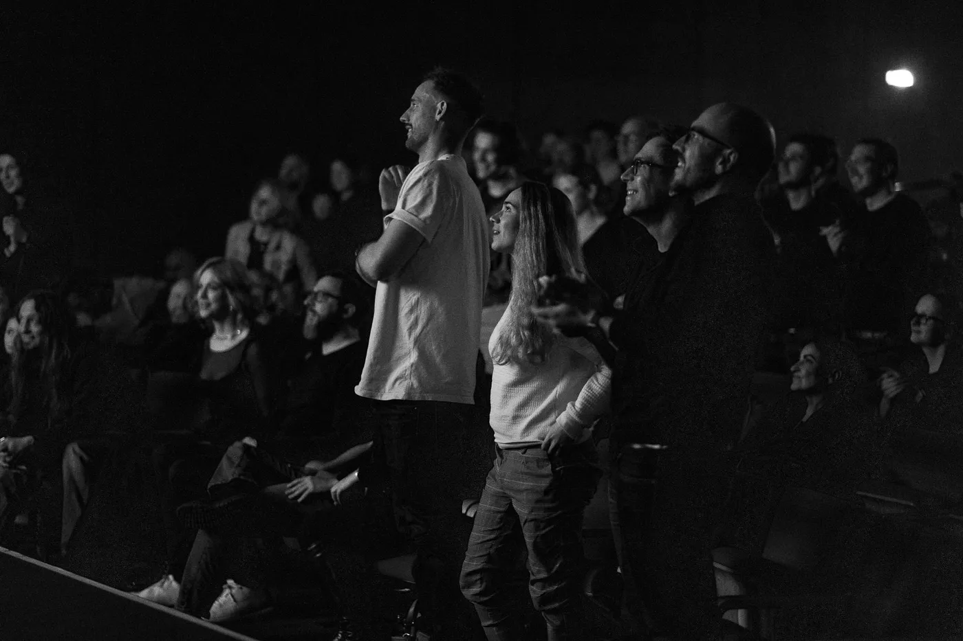 Two audience members on their feet in the dark auditorium
