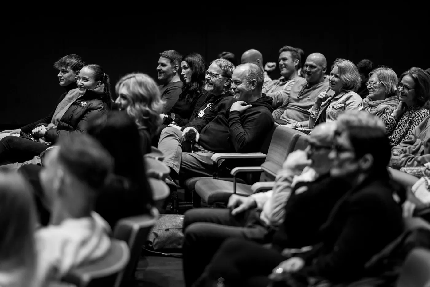 Rows of faces mid-laugh, seen across the seats from the front
