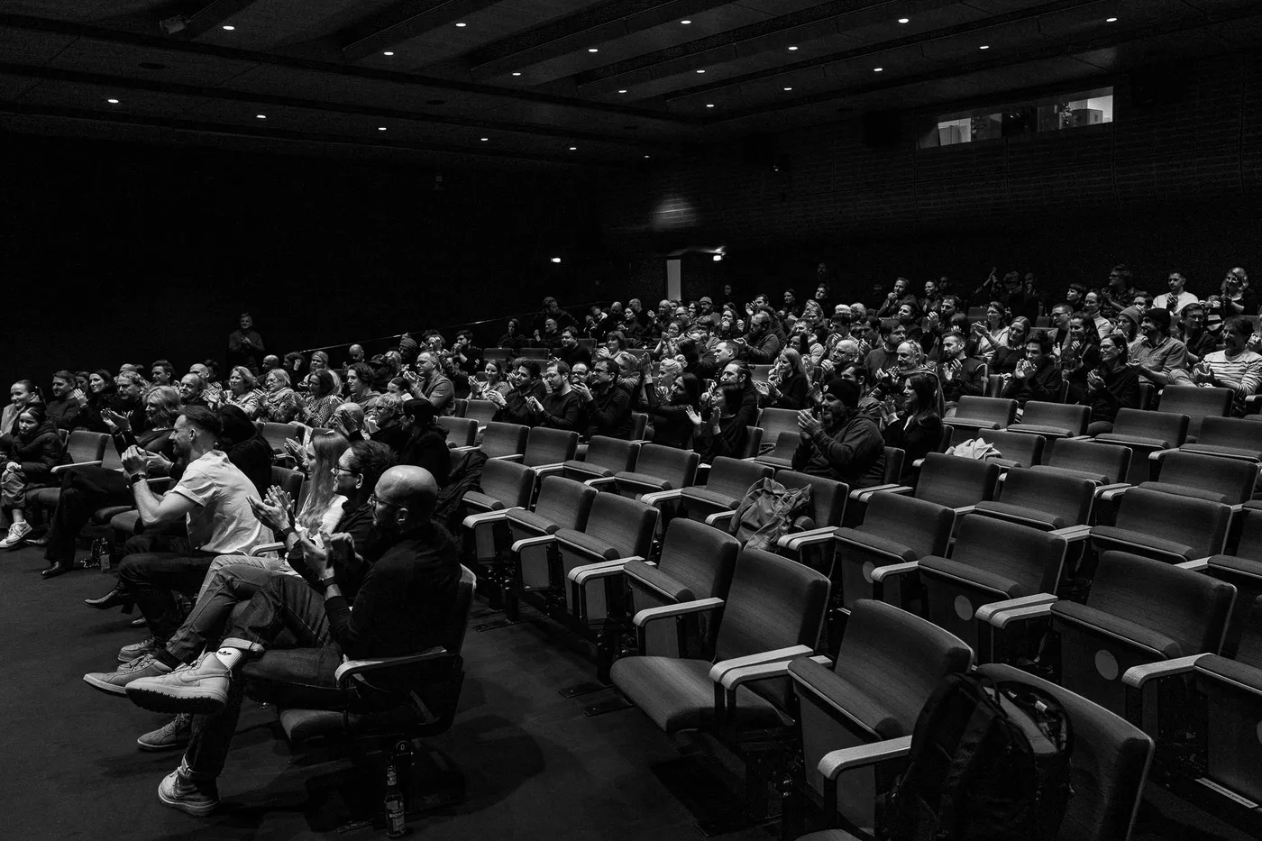 The dark hall from the side, empty seats in the foreground and the audience beyond them