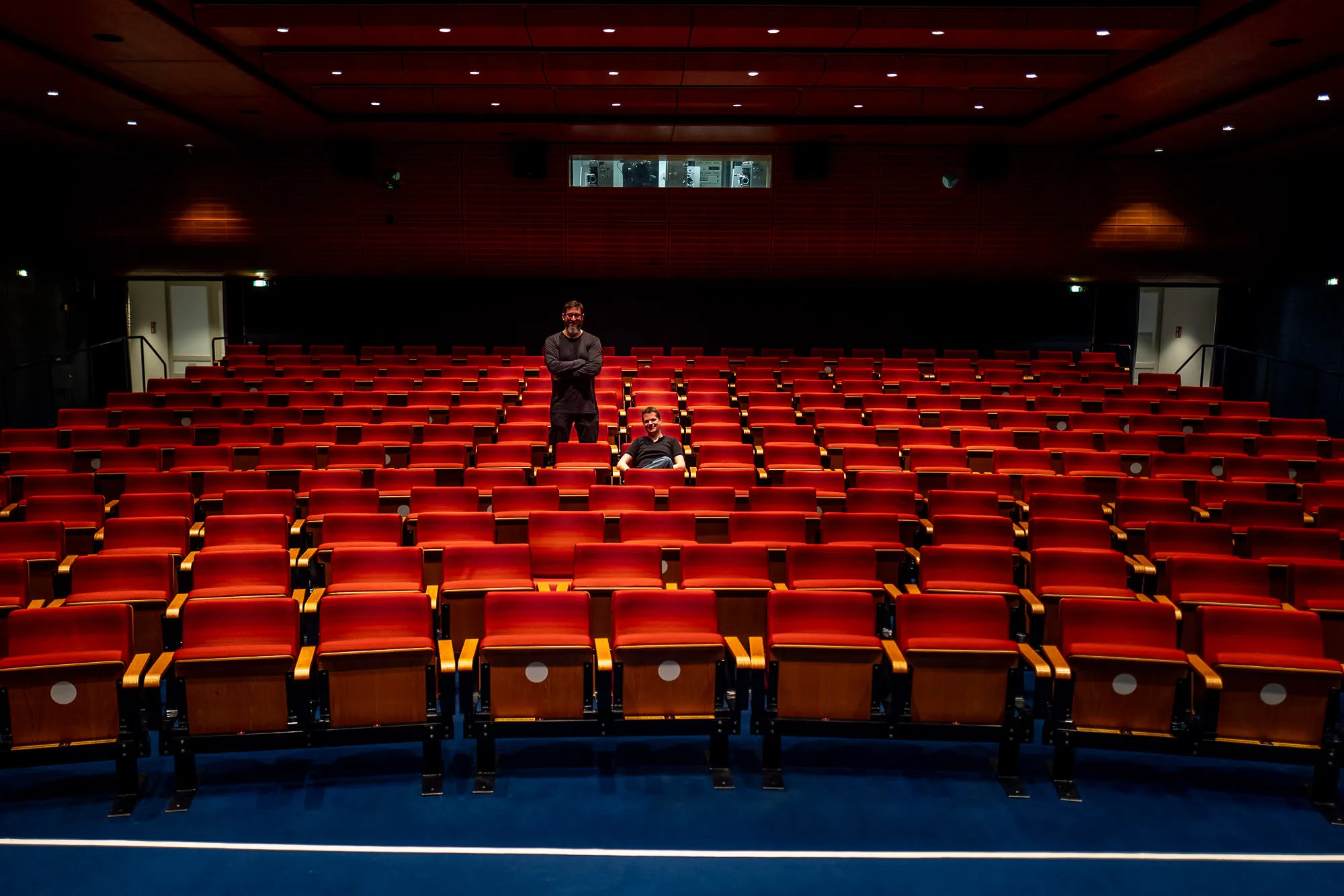 Stefan Nitzsche and Nicolas Schuele alone in an empty cinema, rows of red fold-down seats around them